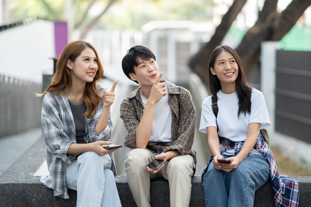 Group of happy students point into the same direction, seeing their friend, sitting in front of the